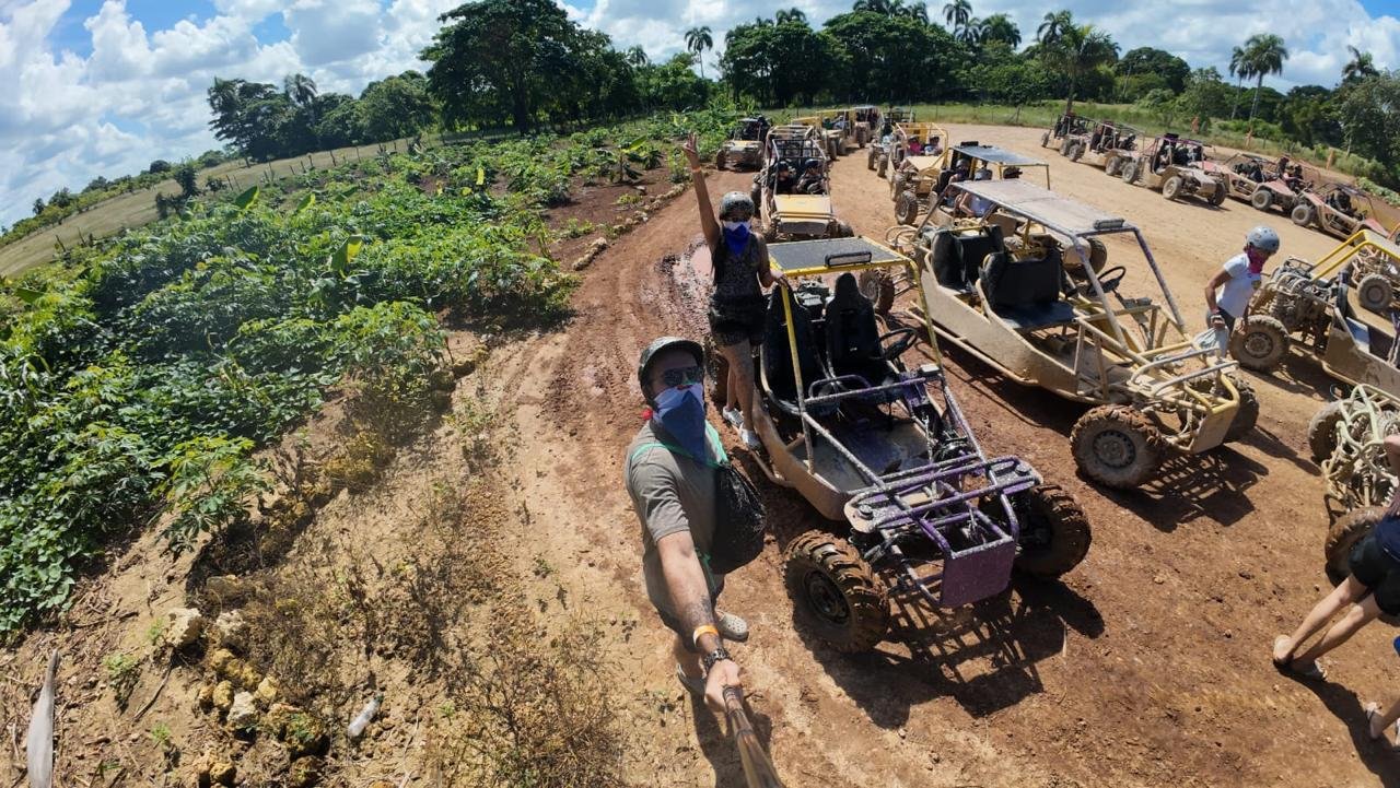 A line of buggies on a dirt track, with a traveller waving at the camera