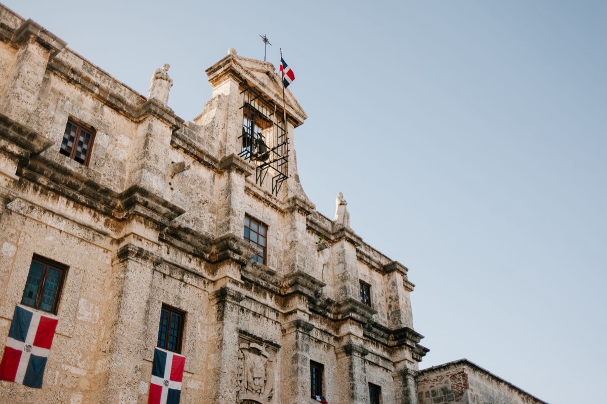 The stone façade of a colonial building flying Dominican flags