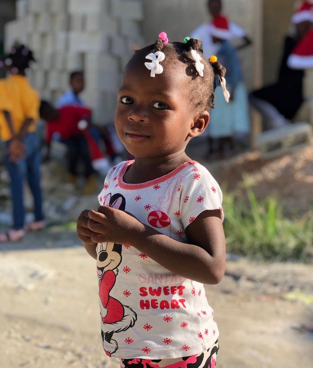 A little girl with hair bobbles smiles in the yard